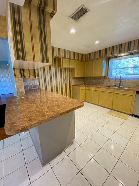 kitchen featuring light tile patterned flooring, a kitchen bar, stainless steel dishwasher, and sink