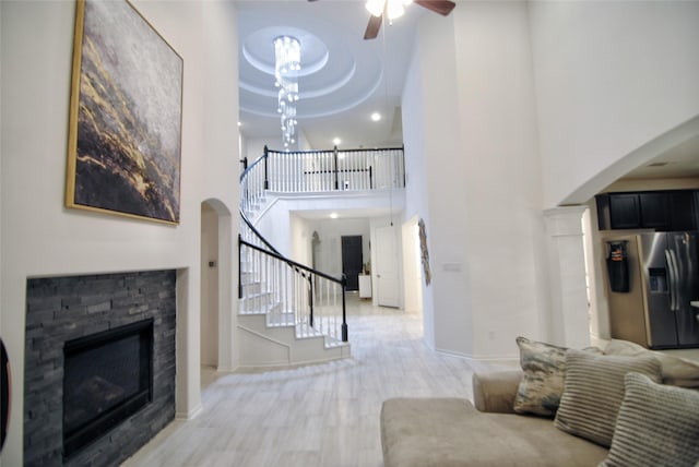 living room with ceiling fan, a stone fireplace, light wood-type flooring, and a high ceiling