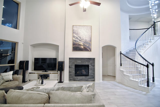 living room with a stone fireplace, ceiling fan, and a towering ceiling