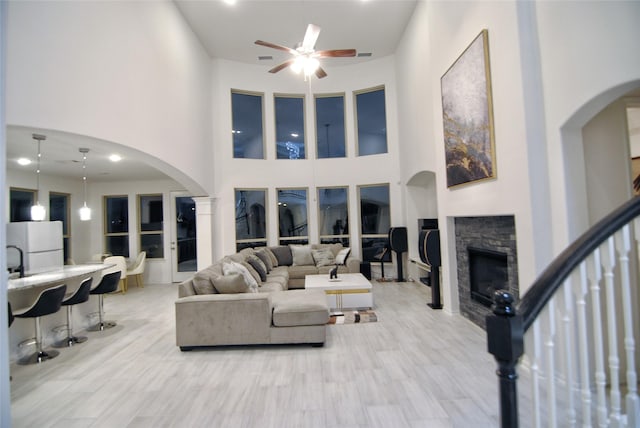 living room with a stone fireplace, ceiling fan, and a towering ceiling