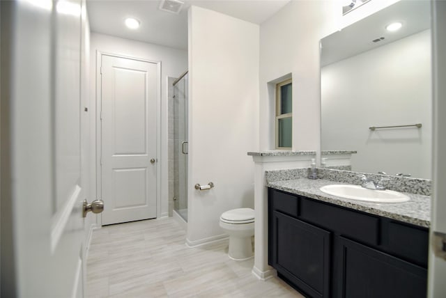 bathroom featuring vanity, a shower with shower door, and toilet