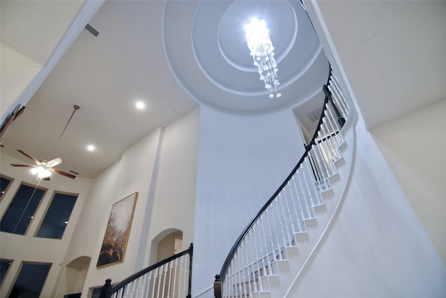 stairs featuring a towering ceiling and ceiling fan with notable chandelier