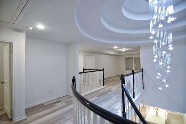 corridor with a chandelier, wood-type flooring, and a raised ceiling