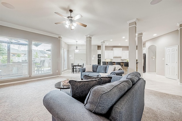 living room featuring ceiling fan with notable chandelier, crown molding, ornate columns, and light carpet