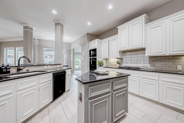 kitchen featuring black appliances, sink, dark stone countertops, white cabinets, and a center island