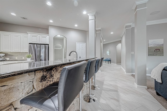 kitchen featuring dark stone counters, white cabinets, stainless steel fridge, ornamental molding, and a kitchen bar