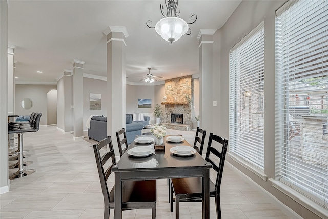 dining room featuring a stone fireplace, ceiling fan, ornamental molding, light tile patterned floors, and decorative columns