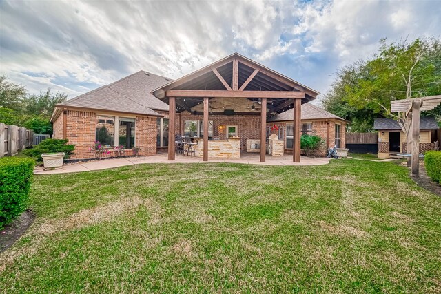 back of property with a lawn, a patio, ceiling fan, and an outdoor kitchen