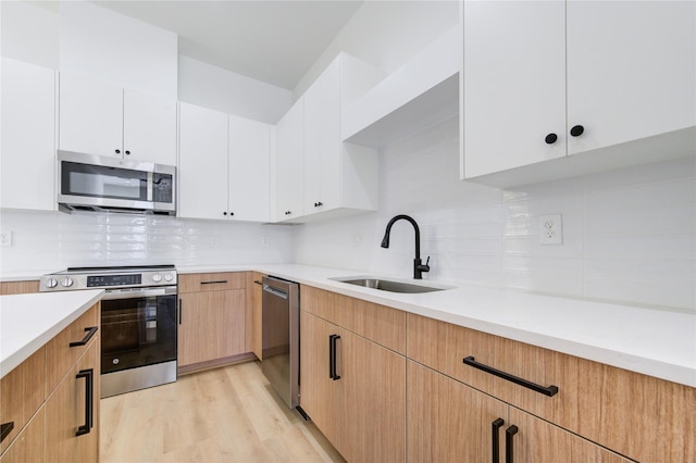 kitchen featuring light wood-type flooring, backsplash, stainless steel appliances, sink, and white cabinets