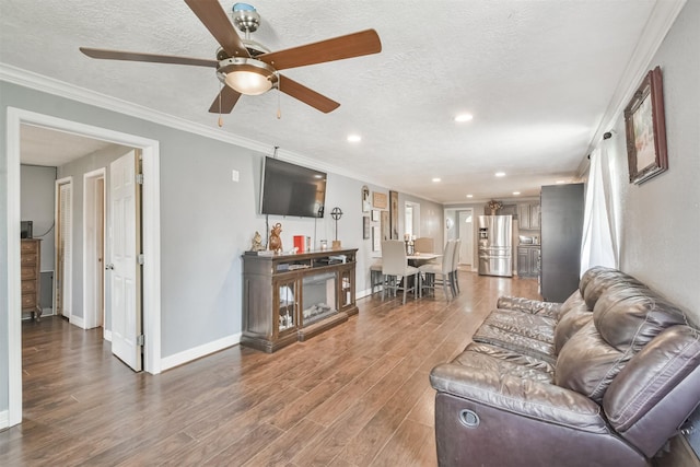 living room with wood-type flooring, a textured ceiling, ceiling fan, and ornamental molding