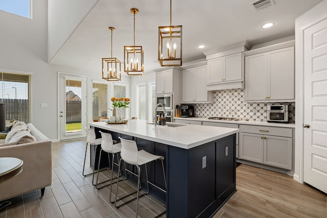 kitchen featuring pendant lighting, a kitchen island with sink, a kitchen breakfast bar, sink, and built in microwave