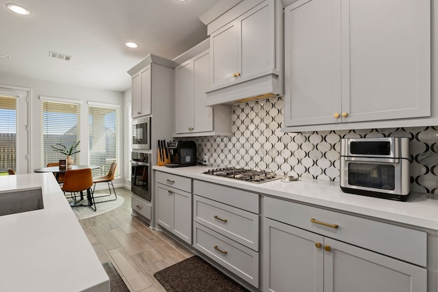 kitchen with sink, stainless steel appliances, premium range hood, light hardwood / wood-style floors, and decorative backsplash