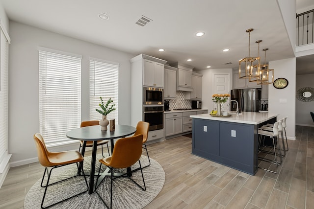 kitchen with a kitchen island with sink, a kitchen breakfast bar, hanging light fixtures, decorative backsplash, and appliances with stainless steel finishes