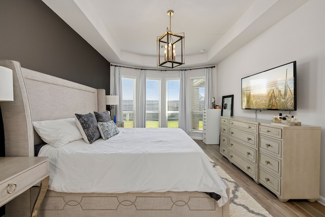 bedroom with a notable chandelier, a raised ceiling, and light hardwood / wood-style flooring