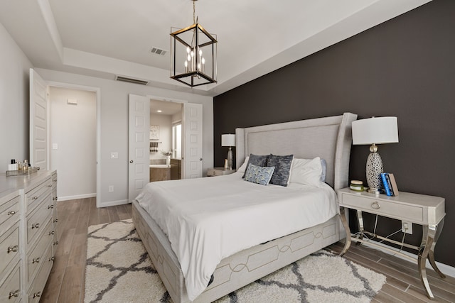 bedroom with ensuite bathroom, an inviting chandelier, and light hardwood / wood-style floors