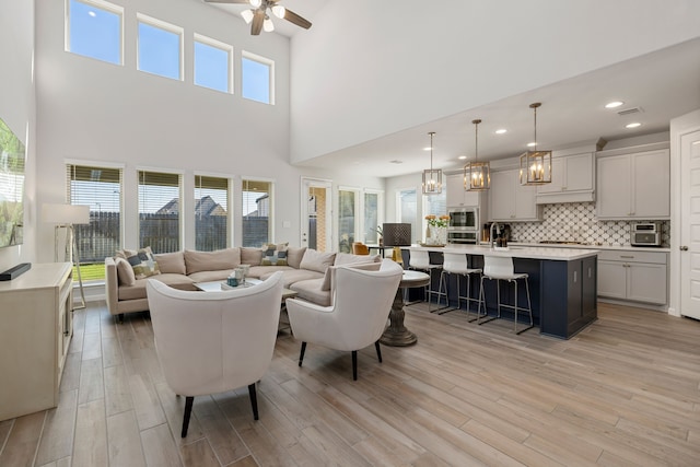 living room featuring ceiling fan, light hardwood / wood-style flooring, a towering ceiling, and a healthy amount of sunlight