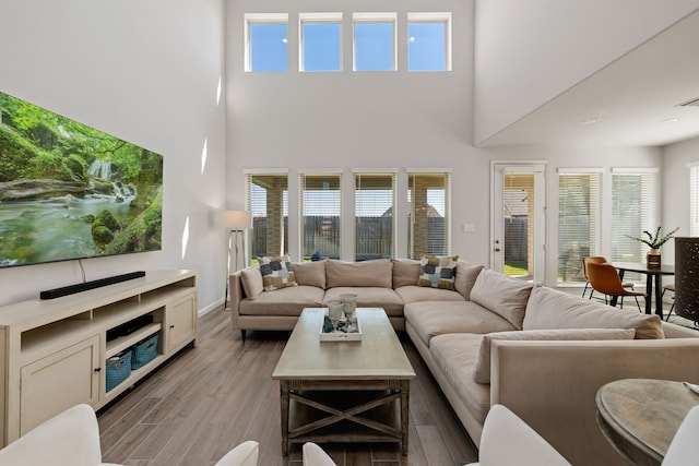 living room featuring a wealth of natural light, a towering ceiling, and light hardwood / wood-style floors