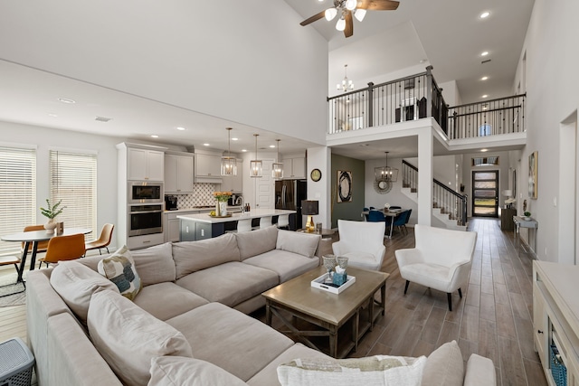 living room featuring ceiling fan with notable chandelier, wood-type flooring, and a towering ceiling