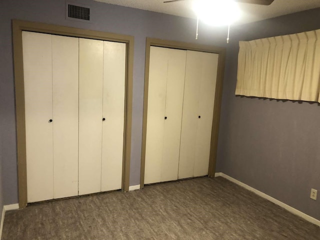 unfurnished bedroom featuring ceiling fan, dark wood-type flooring, and two closets