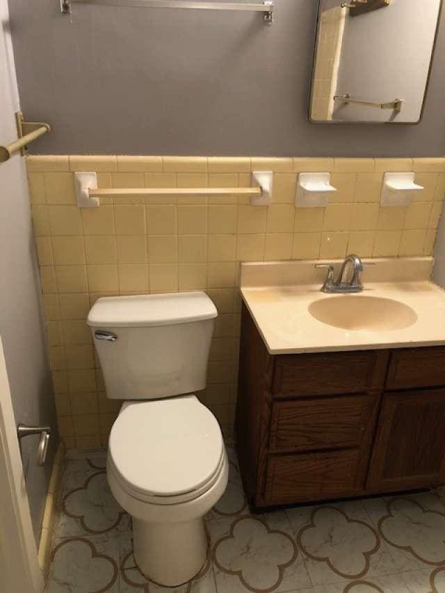 bathroom featuring tile patterned flooring, vanity, toilet, and tile walls