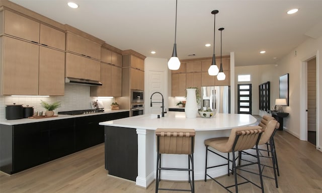 kitchen featuring light brown cabinetry, an island with sink, appliances with stainless steel finishes, and light hardwood / wood-style flooring