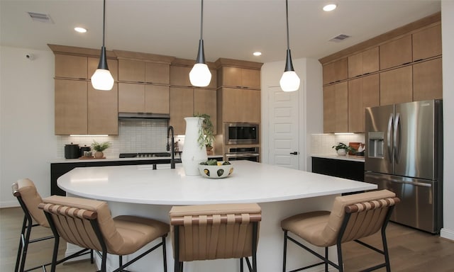 kitchen featuring decorative light fixtures, stainless steel appliances, and an island with sink