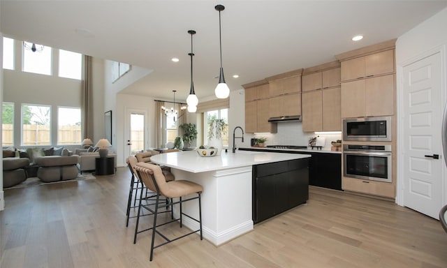 kitchen with stainless steel oven, a kitchen island with sink, light brown cabinetry, and built in microwave