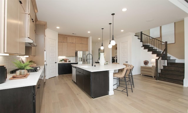 kitchen with a large island with sink, hanging light fixtures, light hardwood / wood-style flooring, light brown cabinetry, and stainless steel fridge with ice dispenser