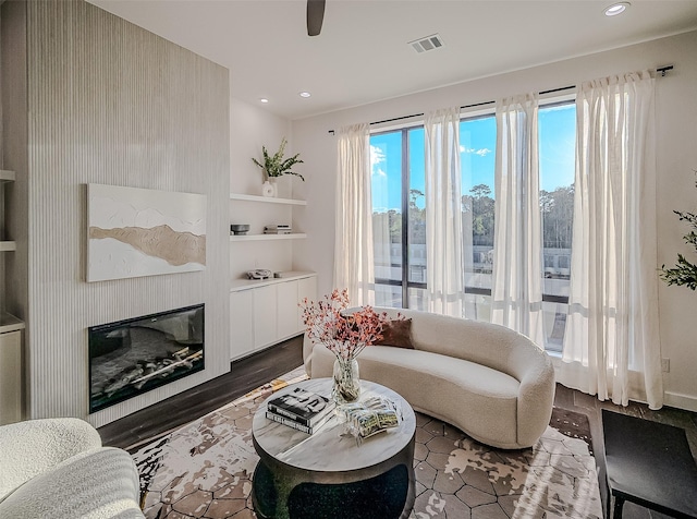 living room featuring ceiling fan, built in features, and a large fireplace