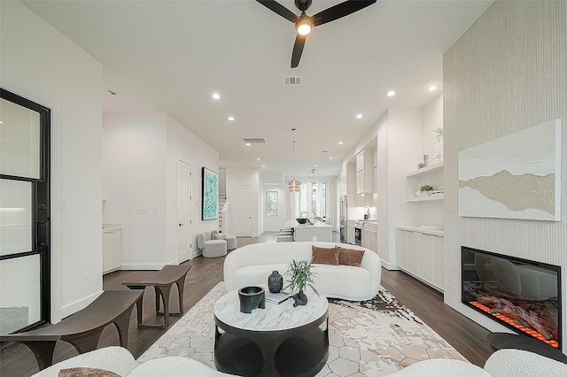 living room with dark wood-type flooring, ceiling fan, a large fireplace, and built in features