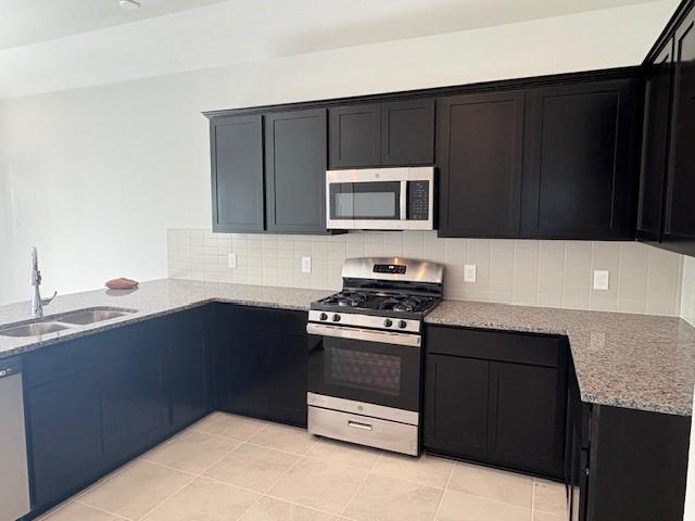 kitchen with decorative backsplash, stainless steel appliances, light stone counters, and sink