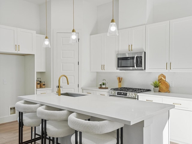 kitchen with stainless steel appliances, white cabinetry, and an island with sink