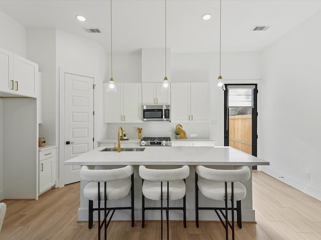 kitchen with a center island with sink, pendant lighting, and white cabinetry