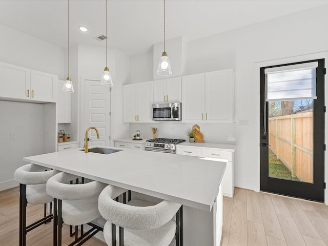 kitchen featuring sink, stainless steel appliances, hanging light fixtures, and an island with sink