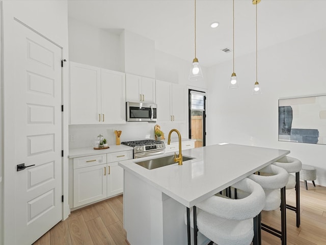 kitchen with a kitchen island with sink, white cabinets, sink, hanging light fixtures, and stainless steel appliances