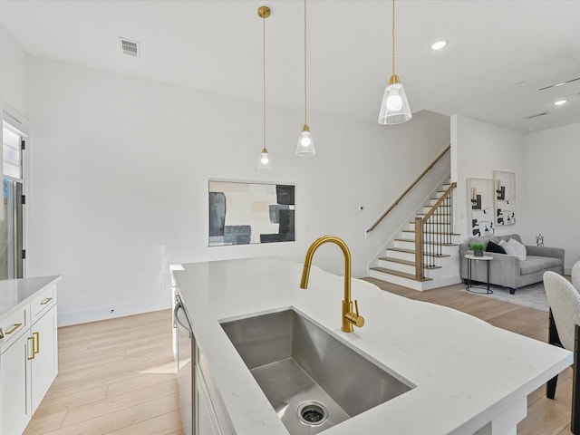 kitchen with decorative light fixtures, white cabinetry, sink, and light hardwood / wood-style flooring