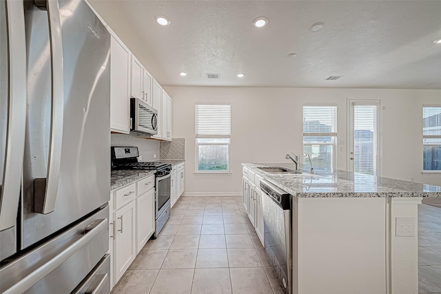 kitchen featuring a center island with sink, white cabinets, sink, light stone countertops, and stainless steel appliances