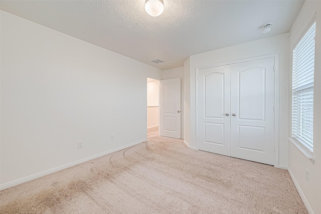 unfurnished bedroom featuring light carpet, a closet, and a textured ceiling