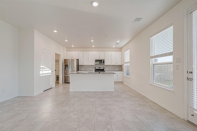 kitchen featuring light stone countertops, stainless steel appliances, a kitchen island with sink, light tile patterned floors, and white cabinets