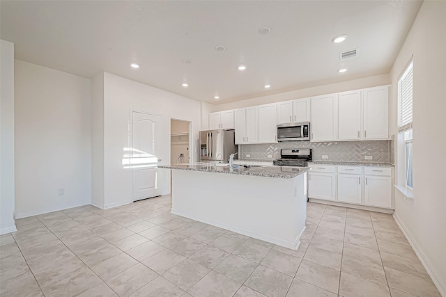 kitchen with white cabinets, light stone countertops, stainless steel appliances, and an island with sink