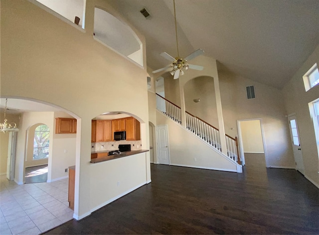 kitchen with a high ceiling, ceiling fan with notable chandelier, light hardwood / wood-style flooring, and black appliances