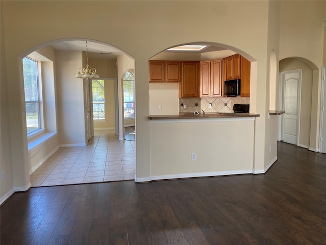 kitchen featuring hardwood / wood-style floors, black appliances, tasteful backsplash, decorative light fixtures, and a chandelier