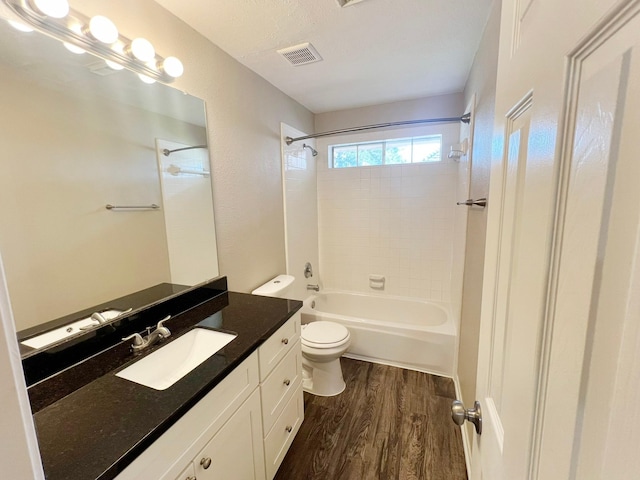 full bathroom with vanity, hardwood / wood-style flooring, tiled shower / bath combo, toilet, and a textured ceiling