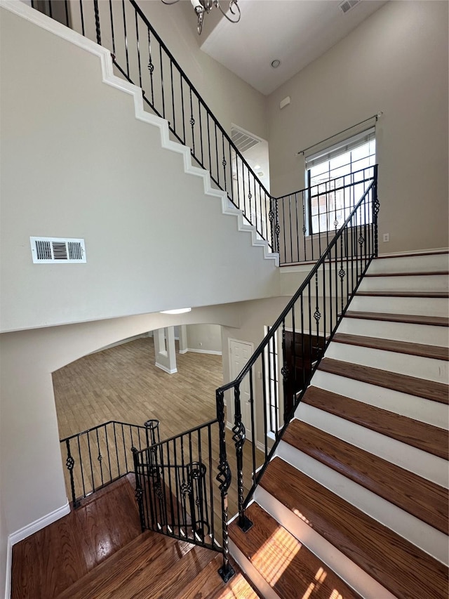 stairs with wood-type flooring, a notable chandelier, and a high ceiling