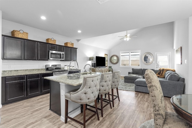 kitchen featuring a kitchen island with sink, a kitchen breakfast bar, appliances with stainless steel finishes, tasteful backsplash, and light hardwood / wood-style floors