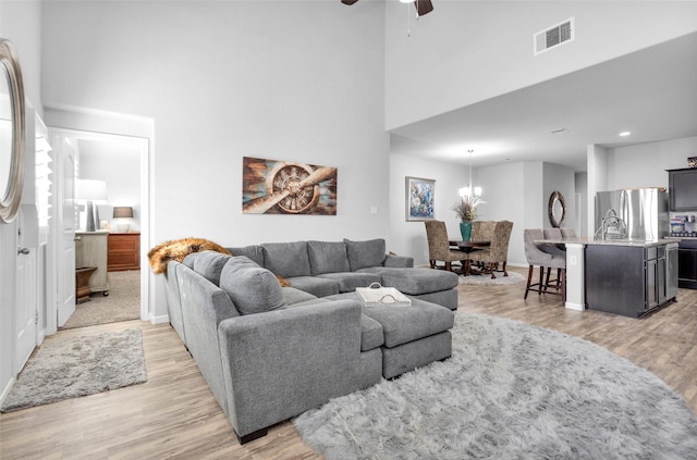 living room with ceiling fan with notable chandelier, light wood-type flooring, and a high ceiling