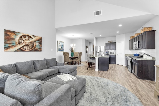 living room featuring sink, light hardwood / wood-style floors, and vaulted ceiling