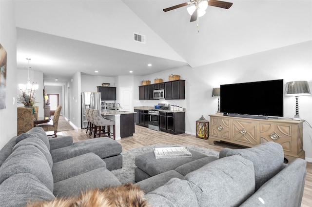 living room with sink, high vaulted ceiling, ceiling fan with notable chandelier, and light wood-type flooring