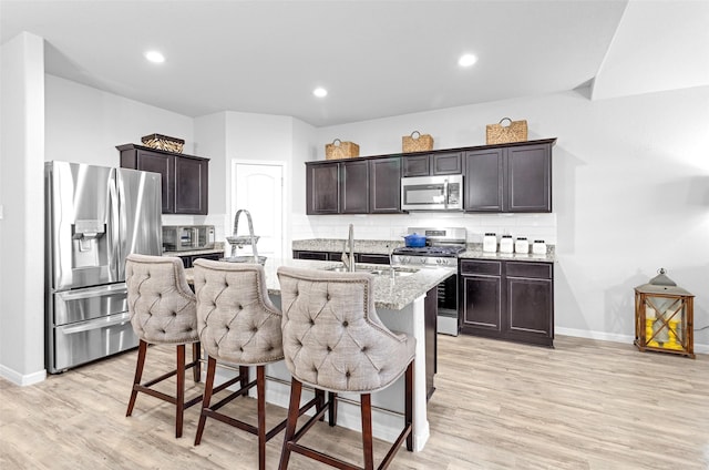 kitchen featuring light stone countertops, appliances with stainless steel finishes, backsplash, a kitchen breakfast bar, and an island with sink