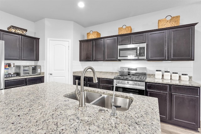 kitchen with decorative backsplash, light stone counters, sink, and appliances with stainless steel finishes